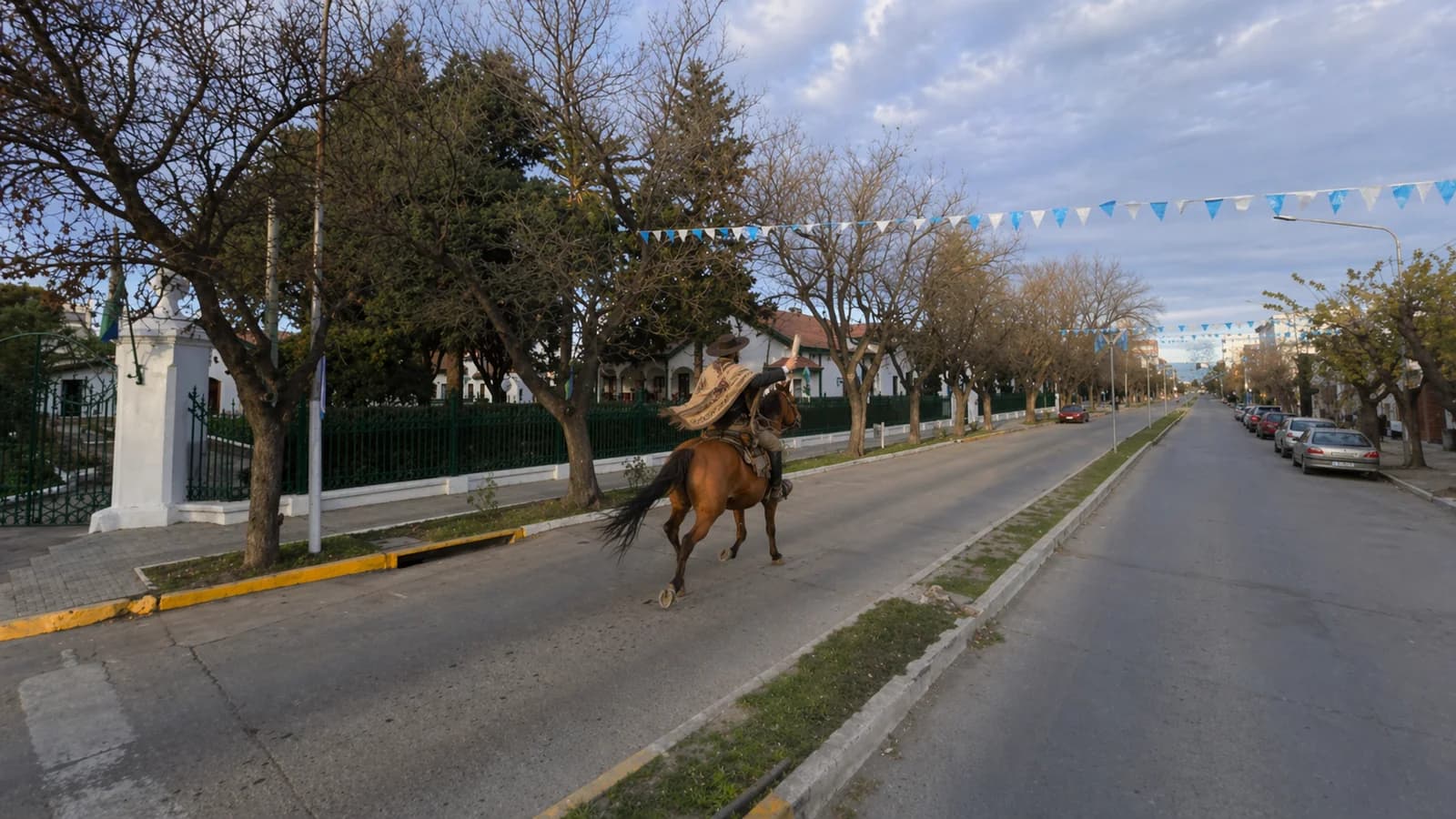 Chasqui a caballo galopando por Av. 25 de Mayo de Viedma · guirnaldas celestes y blancas